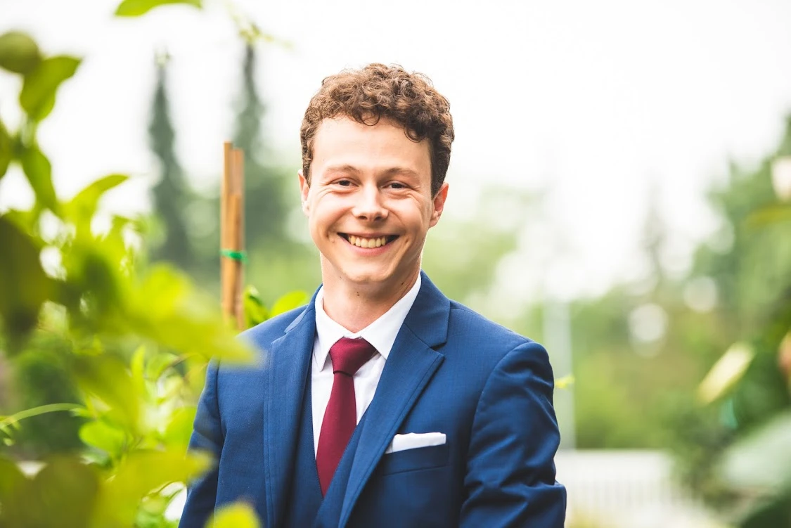 Jonny Woolley in a suit, smiling among greenery